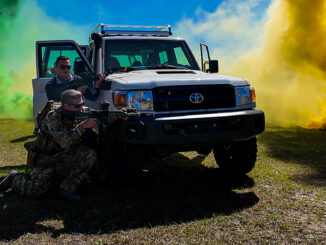 A civilian guest of U.S. Army Special Operations Command (USASOC) takes cover behind a vehicle with a member of USASOC during a Capability Exercise (CAPEX) at Fort Liberty earlier this month. Capability Exercise 2024 is a week-long demonstration and immersive experience of the Army Special Operations Forces’ capabilities and equipment. SSG Gavin Lewis / U.S. Army